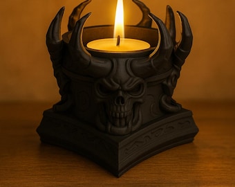 May include: Black candle holder with a skull design and curved horns. The candle holder has a lit, round candle in the center. The candle holder is on a wooden surface.