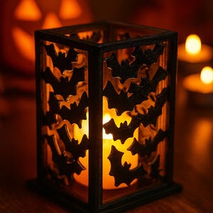 May include: Black, square candle holder with bat cutouts. A lit candle inside casts a warm glow, enhancing the Halloween theme. The background features a carved pumpkin and additional candles, creating a festive atmosphere.