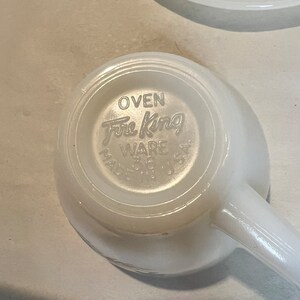 May include: White ceramic mug with a handle. The bottom of the mug has the words "Oven Fire King Ware" printed on it.