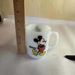Pu&ograve; includere: Una tazza bianca e piccola con Topolino. La tazza ha un manico e una grafica colorata di Topolino. La tazza &egrave; alta circa 7,6 cm.