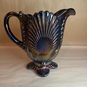 May include: A iridescent purple glass creamer with a scalloped design and a three-pronged base.