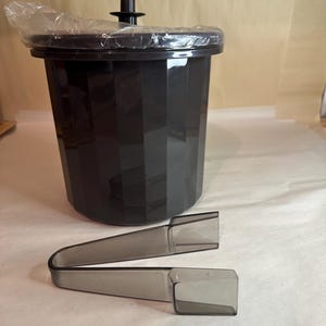 Può includere: Un secchiello per il ghiaccio in plastica nera con un coperchio e una pinza per il ghiaccio in plastica trasparente. Il secchiello per il ghiaccio ha un design a coste.
