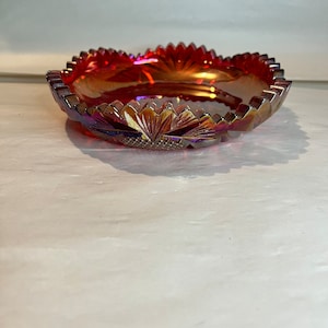 May include: A red iridescent glass bowl with a scalloped edge and a floral design. The bowl is made of carnival glass.