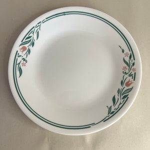 Puede incluir: Plato de cena de cerámica blanca con un diseño floral verde y rosa. El diseño presenta un patrón repetitivo de hojas, flores y tulipanes.