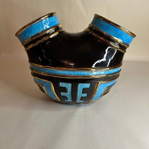 May include: A black and blue ceramic vase with a unique, curved design. The vase features gold trim and geometric patterns in light blue. The vase has a glossy finish and a distinctive shape, suitable for decorative purposes.