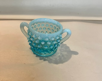 Puede incluir: Un azucarero pequeño de cristal azul claro con dos asas. El cuenco tiene un patrón de clavos y un brillo claro e iridiscente. Este azucarero vintage es probablemente de principios o mediados del siglo XX.