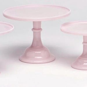 Puede incluir: Conjunto de cuatro soportes para tartas de vidrio rosa de diferentes tamaños. Los soportes son redondos y tienen una base de pedestal.