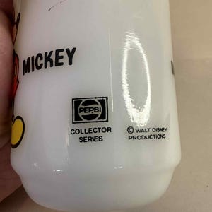Pu&ograve; includere: Bicchiere bianco Pepsi Collector Series con grafica di Mickey Mouse. Il bicchiere presenta il logo Pepsi e il testo "Collector Series". Il testo "Mickey" &egrave; visibile in nero. Il fondo del bicchiere riporta la scritta "Walt Disney Productions".