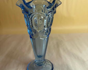 Puede incluir: Un jarrón de cristal azul claro con un borde con volantes y una base acampanada. El jarrón tiene un patrón detallado de lunas crecientes y estrellas. El jarrón mide aproximadamente 20 cm de alto.