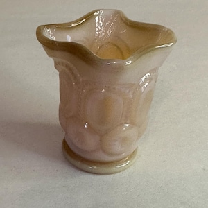 May include: A small, pale pink glass vase with a scalloped rim and a textured, raised pattern. The vase has a slightly iridescent finish.