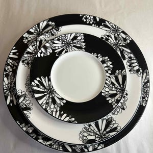 Puede incluir: Un conjunto de tres platos de cerámica con un diseño floral en blanco y negro. El plato más grande tiene un borde blanco con patrones florales negros. El plato del medio es negro con patrones florales blancos. El plato más pequeño es blanco.