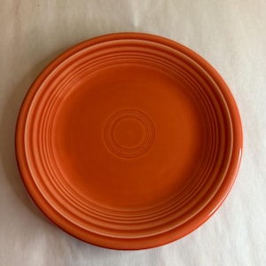 Puede incluir: Un plato de cena de cerámica naranja brillante con un borde blanco y círculos concéntricos en el centro.