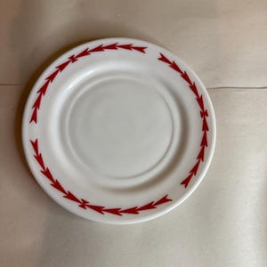 Puede incluir: Un plato de cerámica blanco con un diseño de flechas rojas alrededor del borde. El plato tiene un diseño simple y limpio, adecuado para el uso diario. Las flechas rojas crean un borde decorativo.