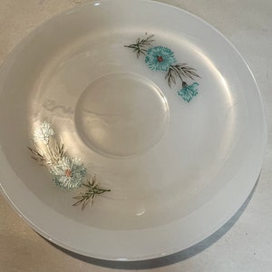 May include: White saucer with a floral design featuring blue flowers and green leaves.