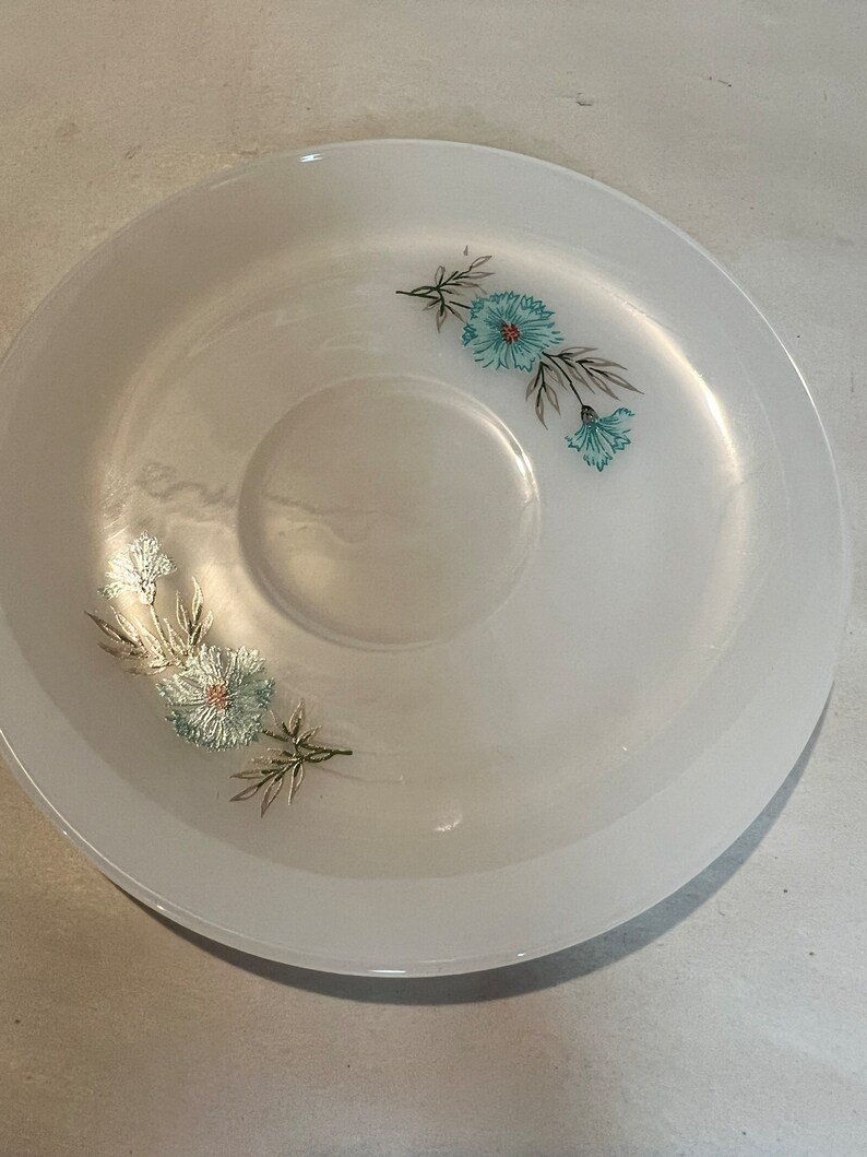 May include: White saucer with a floral design featuring blue flowers and green leaves.