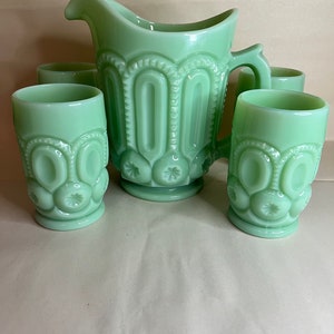May include: A vintage green glass jug and matching glasses set. The jug has a handle and a decorative pattern of stars and arches. The glasses have a similar design. The set is made of opaque glass, likely from the mid-20th century.