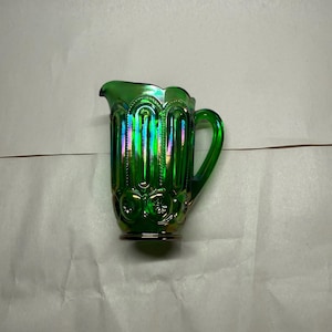 Könnte beinhalten: Grüner Glaskrug mit Henkel und Ausguss. Der Krug hat ein Stern- und Monddesign und ein schillerndes Finish. Der Vintage-Krug eignet sich zum Servieren von Getränken. Höhe ca. 15 cm.
