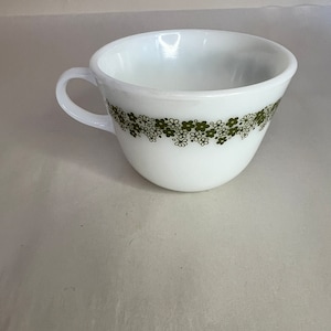 May include: A white ceramic teacup with a green floral pattern around the rim.