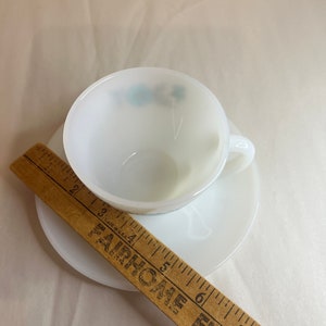 May include: White ceramic teacup and saucer set with a blue floral design. The saucer is 5.5 inches in diameter.
