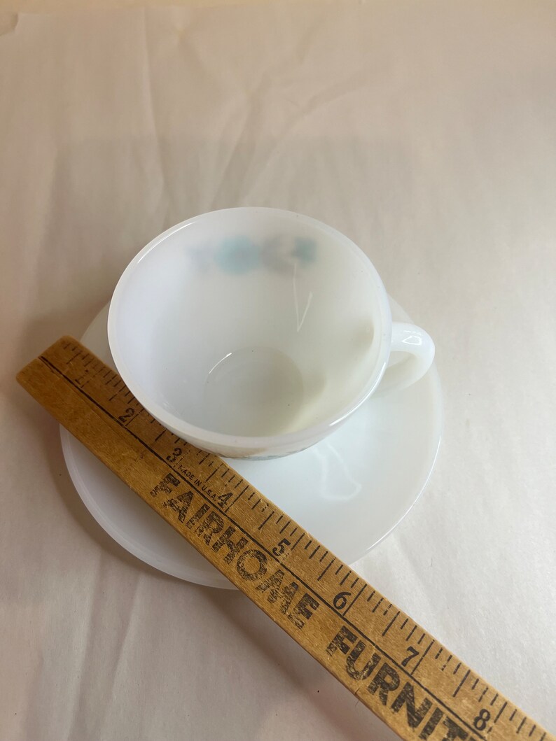 May include: White ceramic teacup and saucer set with a blue floral design. The saucer is 5.5 inches in diameter.