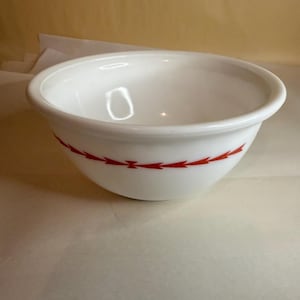 Puede incluir: Cuenco mezclador de cerámica blanca con un diseño de flechas rojas alrededor del exterior. El cuenco tiene forma redondeada y un borde ancho. Este utensilio de cocina es adecuado para mezclar ingredientes.