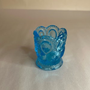 May include: A small, light blue glass toothpick holder with a scalloped rim and a textured, circular pattern.