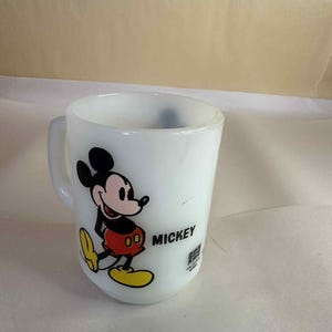 Pu&ograve; includere: Tazza in ceramica bianca con Topolino. Il personaggio dei cartoni animati &egrave; raffigurato in nero, rosso, giallo e bianco. La parola "MICKEY" &egrave; stampata in nero. Un oggetto da collezione Disney vintage.