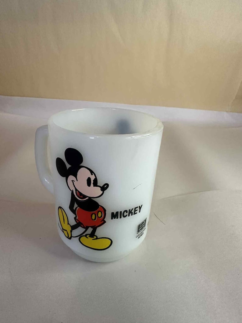 Pu&ograve; includere: Tazza in ceramica bianca con Topolino. Il personaggio dei cartoni animati &egrave; raffigurato in nero, rosso, giallo e bianco. La parola "MICKEY" &egrave; stampata in nero. Un oggetto da collezione Disney vintage.