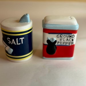 May include: A pair of ceramic salt and pepper shakers. The salt shaker is cylindrical, navy blue with yellow and white stripes, and the word "SALT" in white. The pepper shaker is rectangular, red with a black pepper graphic, and the words "GROUND BLACK PEPPER".