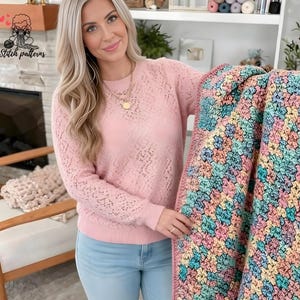 May include: A pastel-colored crochet blanket with a floral pattern is held by a person wearing a light pink sweater. The blanket features a mix of pink, blue, yellow, and green hues. The text "Stitch patterns" is in the upper left corner.