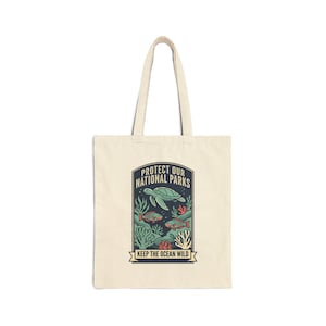 May include: A cream-coloured tote bag with a graphic of a sea turtle, fish, and coral, and the text "PROTECT OUR NATIONAL PARKS" and "KEEP THE OCEAN WILD". The bag has two handles.