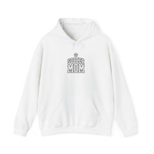 May include: A white long-sleeve hooded sweatshirt featuring a front kangaroo pocket and a drawstring hood. The center of the chest displays a black graphic with the text SOCCER MOM in a collegiate font, topped with a small soccer ball icon.