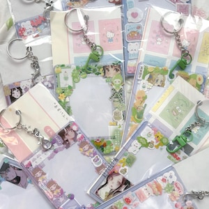 Pode incluir: Uma coleção de chaveiros de plástico transparente com vários designs coloridos. Cada chaveiro apresenta um anel de metal e um pingente decorativo, com adesivos e ilustrações de personagens de anime, comida e outros motivos fofos. Os chaveiros são embalados em plástico transparente.