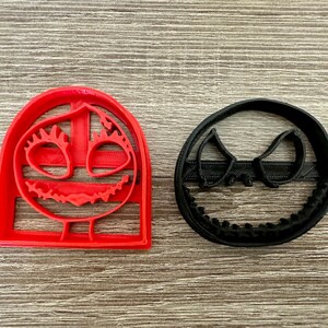 May include: Two cookie cutters, one red and one black, shaped like the faces of Jack Skellington and Sally from the movie The Nightmare Before Christmas.