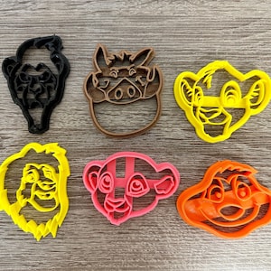 May include: Six plastic cookie cutters in the shapes of characters from The Lion King. The cutters are in various colors, including black, brown, yellow, pink, and orange. The shapes include Simba, Timon, Pumbaa, and others.