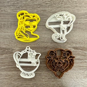 May include: Four cookie cutters featuring characters from the Disney movie Beauty and the Beast. The cutters are yellow, white, and brown. The characters are Belle, the Beast, Mrs. Potts, and Lumiere.