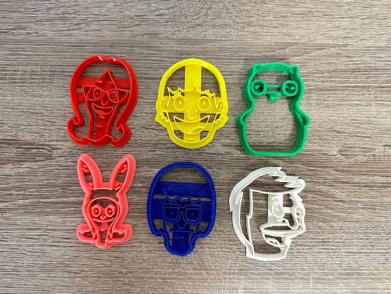 May include: Set of six cookie cutters featuring cartoon characters. The cutters are made of plastic and are in various colors, including red, yellow, green, blue, and white.