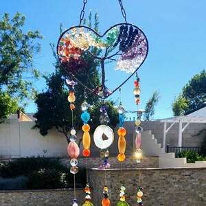 May include: A heart-shaped wire tree of life wind chime with colorful gemstones and agate slices. The chime hangs from a chain and has multiple strands of beads and crystals.