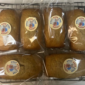 May include: Six individually packaged banana bread loaves with a yellow and red logo that says "Polly Anna Star Bakery" on each loaf.
