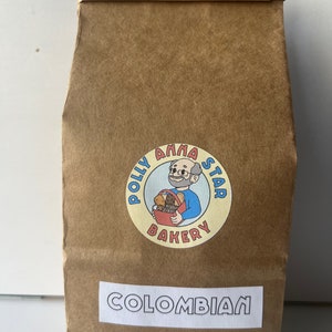 May include: A brown paper bag with a white label that says "COLOMBIAN". The bag has a logo for "Polly Anna Star Bakery" with a cartoon baker holding a basket of bread.