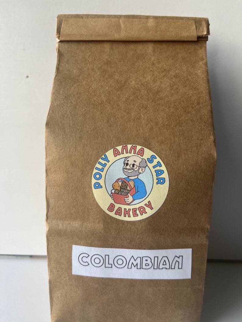 May include: A brown paper bag with a white label that says "COLOMBIAN". The bag has a logo for "Polly Anna Star Bakery" with a cartoon baker holding a basket of bread.