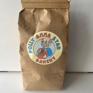 May include: A brown paper bag with a yellow circle logo that says "Polly Anna Star Bakery" with a cartoon illustration of a person holding a basket of baked goods.