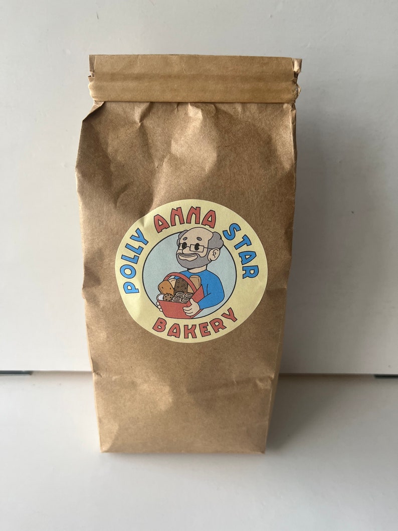 May include: A brown paper bag with a yellow circle logo that says "Polly Anna Star Bakery" with a cartoon illustration of a person holding a basket of baked goods.
