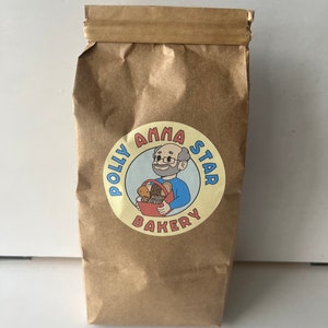 May include: A brown paper bag with a yellow circle logo that says "Polly Anna Star Bakery" with a cartoon illustration of a man holding a basket of bread.
