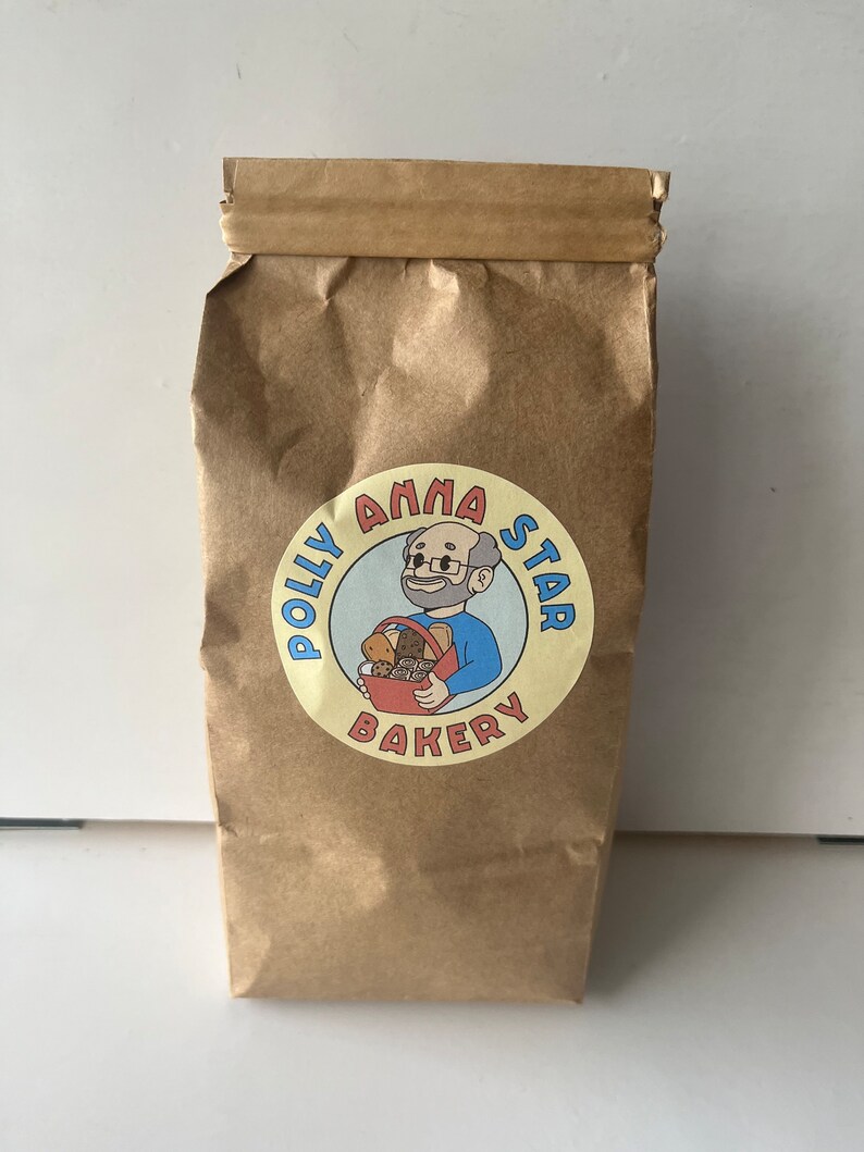 May include: A brown paper bag with a yellow circle logo that says "Polly Anna Star Bakery" with a cartoon illustration of a man holding a basket of bread.
