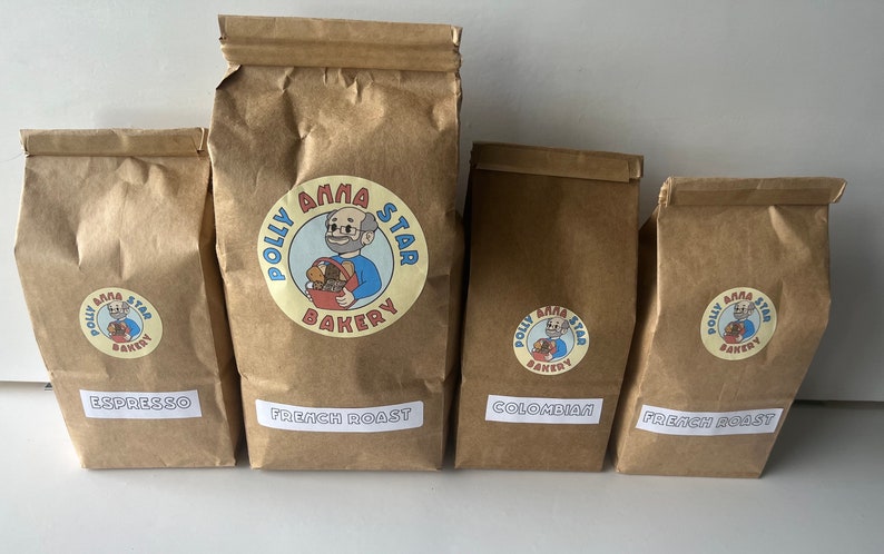 May include: Four brown paper bags with white labels. The bags are labeled with different coffee blends: Espresso, French Roast, Colombian, and French Roast. Each bag has a logo with a cartoon baker and the text "Polly Anna Star Bakery".