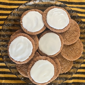 May include: A plate of gingerbread cookies with white frosting. The cookies are round and have a slightly rough texture. The frosting is smooth and white.