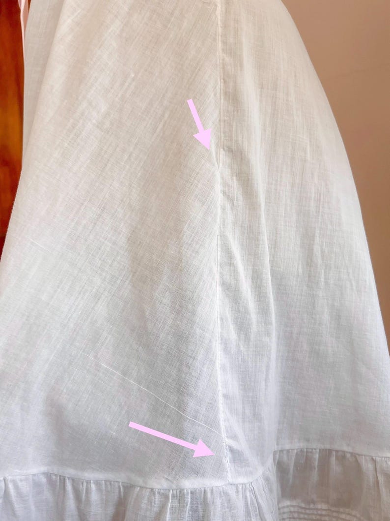 May include: Close-up of a white garment, possibly a dress or skirt, with visible seams and a ruffled hem. The fabric appears to be lightweight, with a subtle texture. The stitching details are prominent, highlighting the garment's construction.