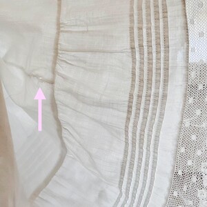 May include: Close-up of a white fabric with a ruffled edge. The fabric has vertical stripes and a delicate lace trim. The texture appears soft and lightweight, with subtle variations in tone.