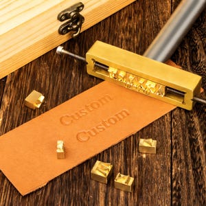 May include: A white ceramic mug with a black handle and the text "But First, Coffee" in a black, bold font. The mug is on a white surface.